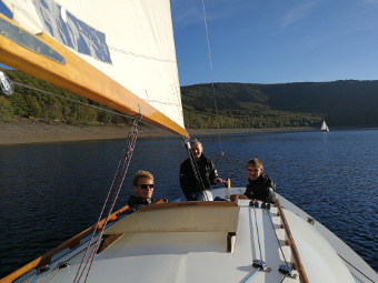 Drei glückliche Menschen segeln mit Folkeboot in der Sonne